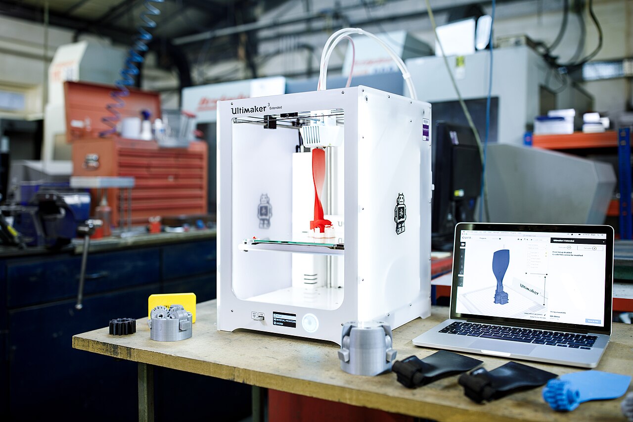 Stampante 3D al lavoro in officina tra prototipi stampati